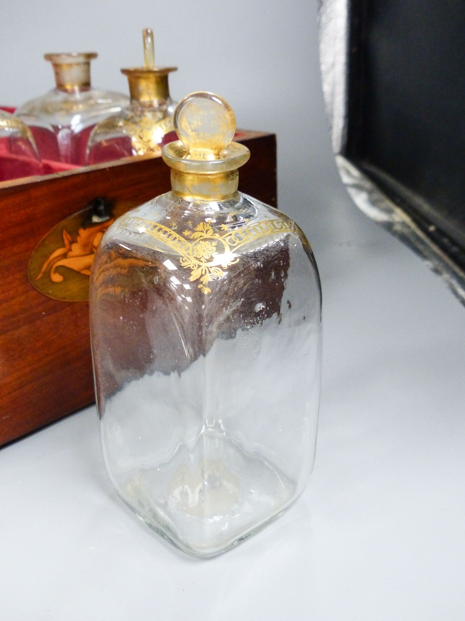 A mahogany inlaid decanter box containing five gilt decorated decanters